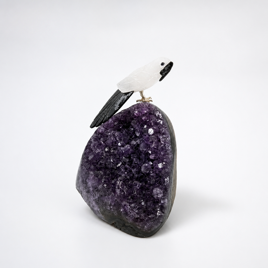 Hand-carved crystal parrot perching on a natural amethyst cluster specimen