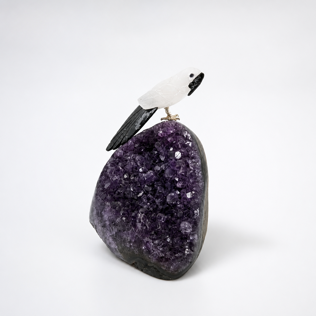 Hand-carved crystal parrot perching on a natural amethyst cluster specimen