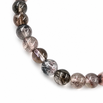 Side view of the 5.5mm Black Super Seven Melody Stone bracelet on a pale surface